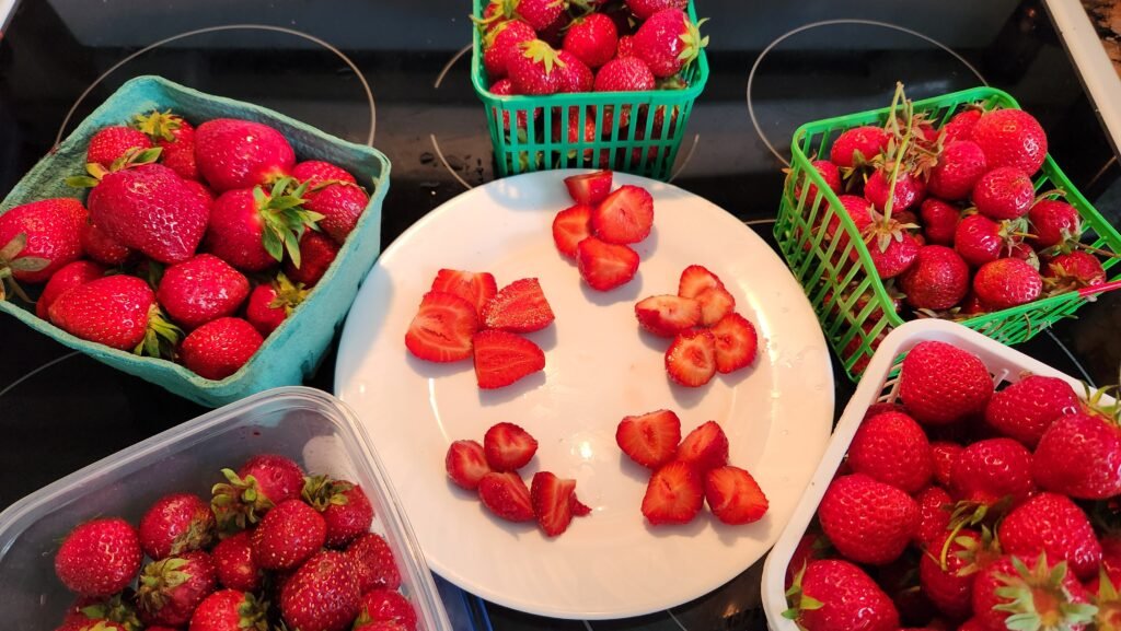 Five baskets of local strawberries from Kingston, Ontario arranged in a circle with a plate of sliced strawberries in the middle.